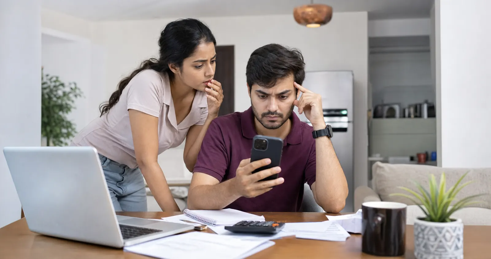 Indian couple reviewing a failed auto-debit notification on a smartphone with bills and laptop on the table